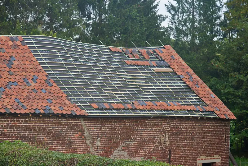 Een hoevedak waarvan de pannen deels vervangen worden