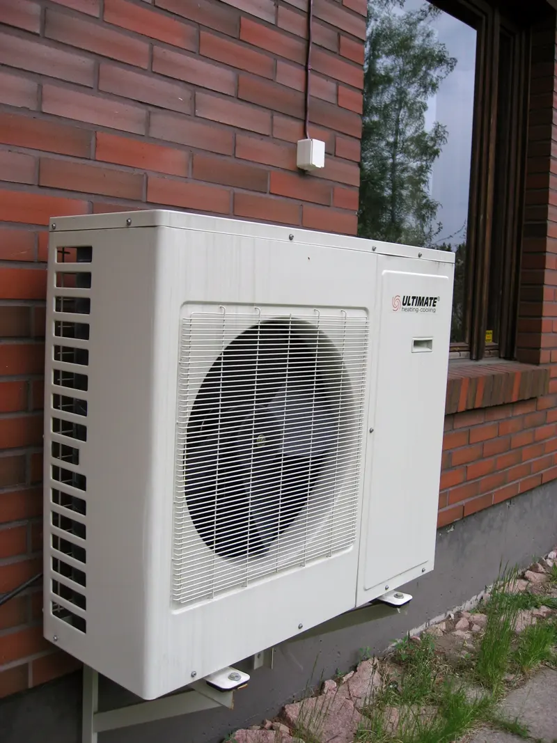 De buitenunit van een warmtepomp tegen een bakstenen gevel