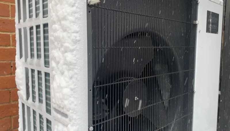 De buitenunit van een warmtepomp met sneeuw op de rooster